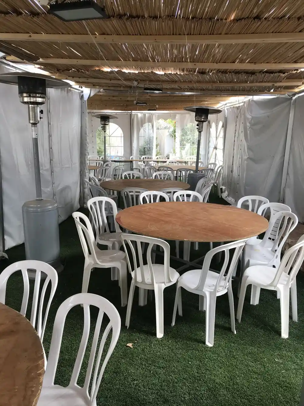 פטריות חימום לצד שולחנות עגולים וכיסאות לבנים במתחם מקורה — חימום לאזור הישיבה באירוע | ARTM — השכרת פטריות חימום באזור התעשייה עמק חפר | ARTM