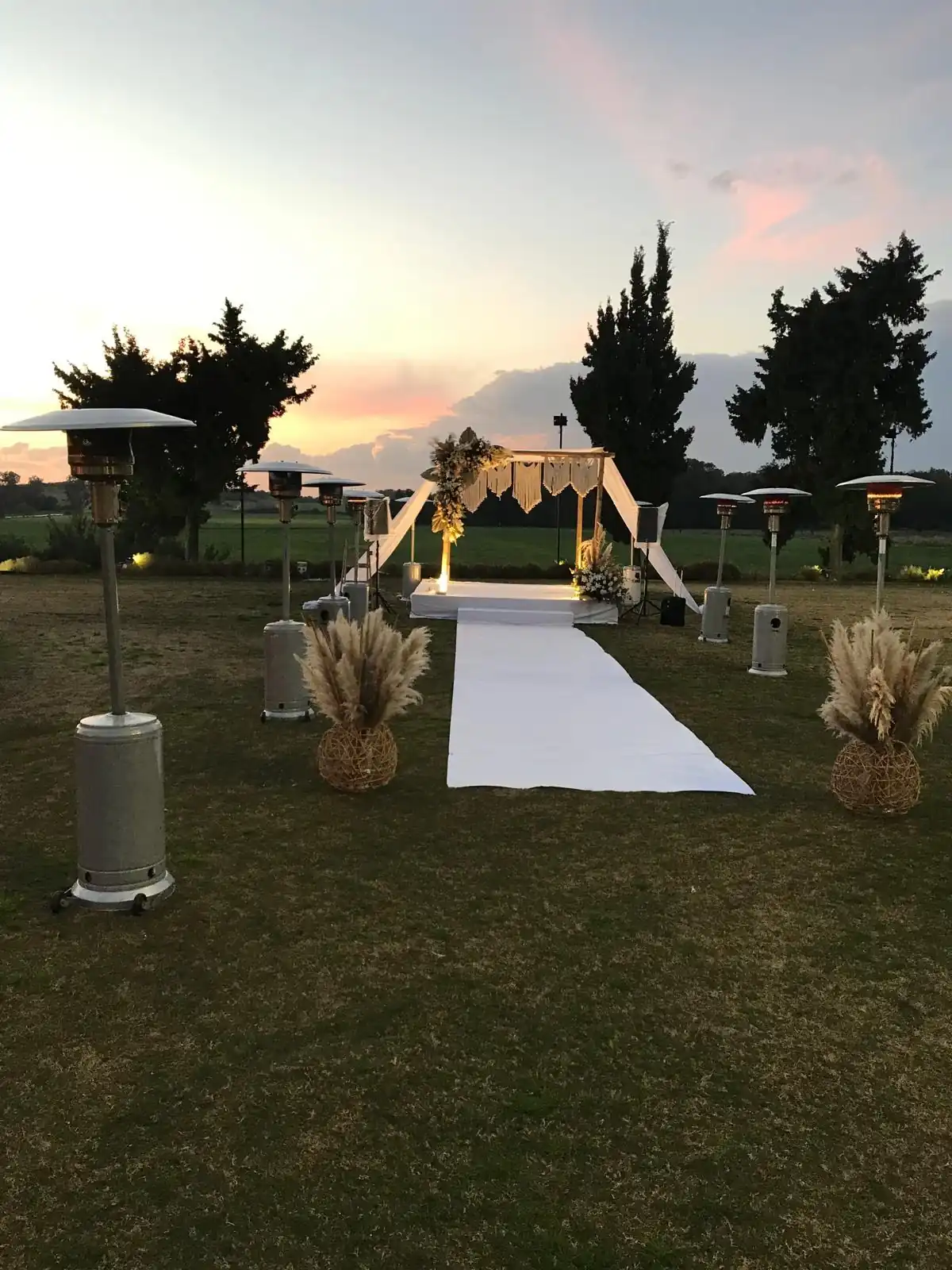 שורת פטריות חימום גז לאורך שביל החופה בשקיעה — השכרת פטריות חימום לחתונת גן | ARTM | ARTM